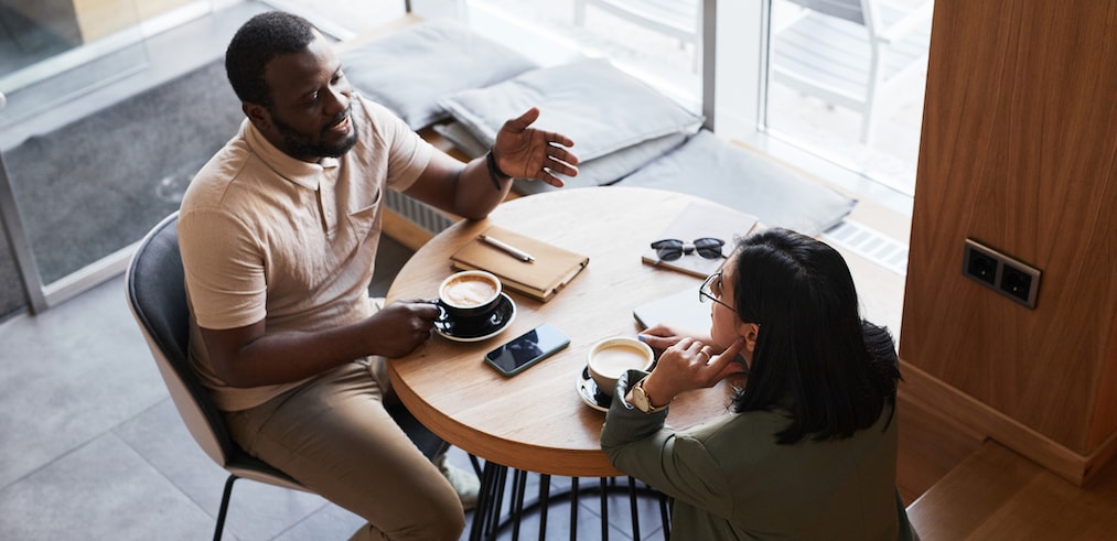 High angle portrait of two young people chatting at table in graphic cafe interior, copy space