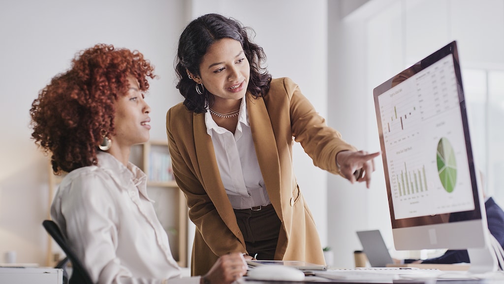 Business people, computer and analytics monitoring corporate statistics of graph or chart on screen at office. Employee women in teamwork collaboration looking at company data or analysis on PC